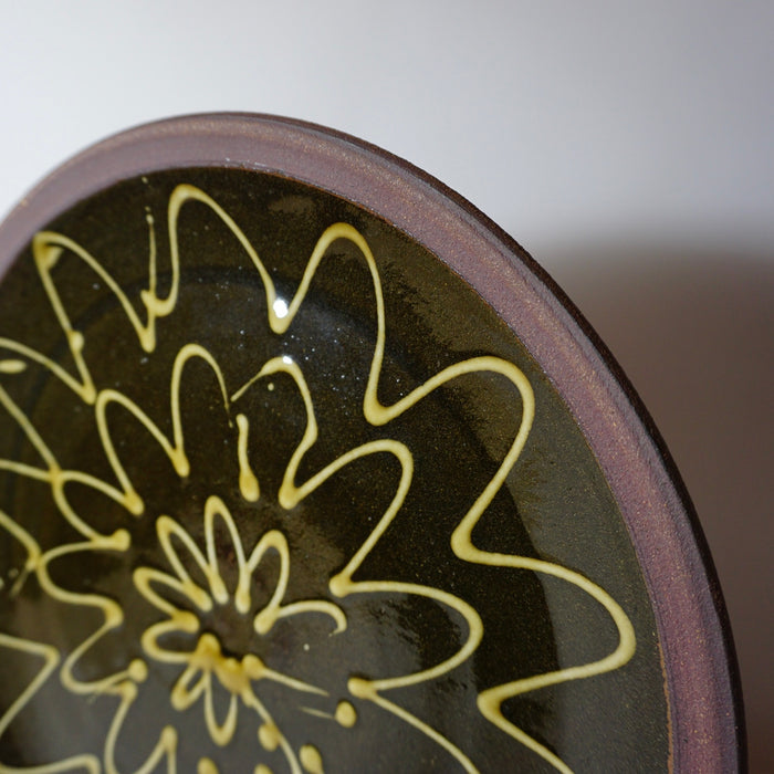 close up detail of the rim of a handmade ceramic plate made from a red clay and with an abstract fluid pattern. 