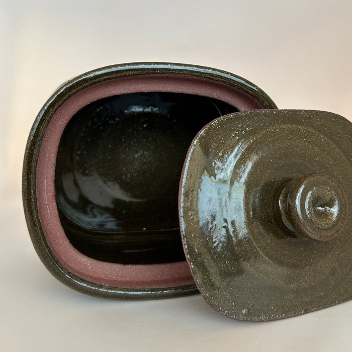 butter dish lying on its side with the lid next to it so you can see the hand made gallery of the lid and the inside of the dish. 