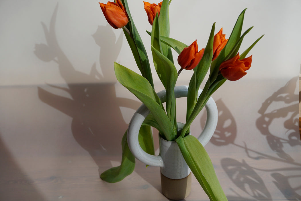 a straight vase with an oversized round handle at the top. and a bunch or red tulips