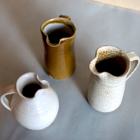 three milk jugs in different colours and shapes on a table. 