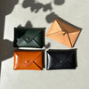 4 small leather wallets in different colours sitting in the sun on a blue table. 