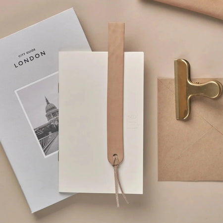 a book mark on a white notebook, a gold bulldog clip and a city guide to London. 