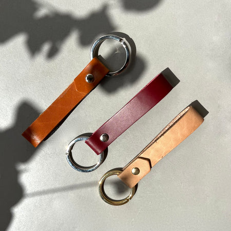 Three leather keyrings on a blue table in the sun. 