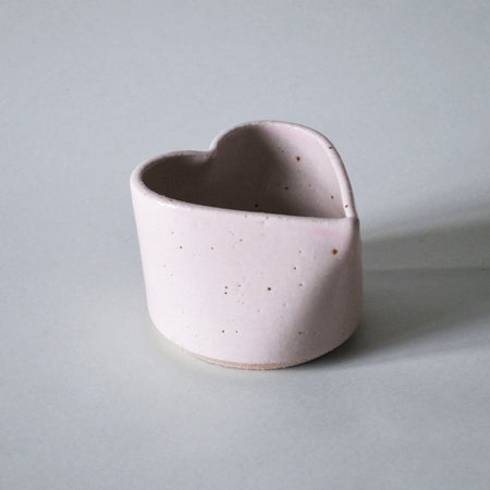 a pink handmade ceramic cup in the shape of a heart by Mae Ceramics. 