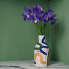 porcelain vase with abstract brushwork pattern and a bunch of iris flowers on a green background. 