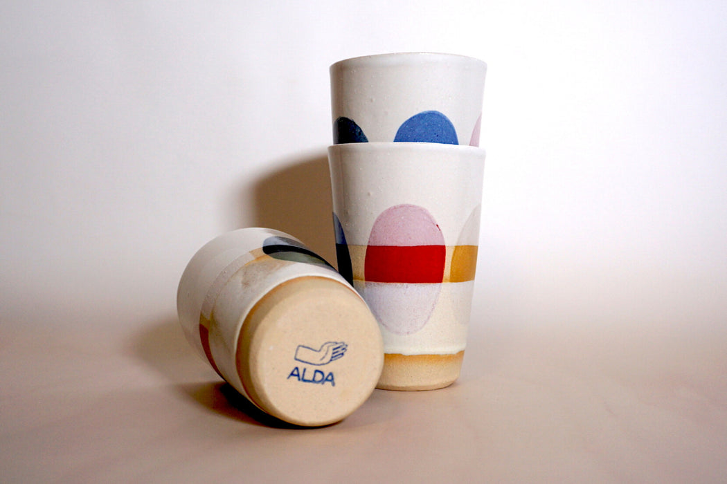 three cups with multi coloured dots painted around the side. one is lying down to show the makers mark of Sophie Alda. 