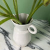 close up of a a white vase with two lugs at the top. sitting on a marble table with a bunch of red poppies. 