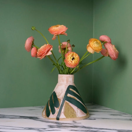 cone shaped vase with a leaf pattern and pinky yellow flowers on a marble table with a green background. 