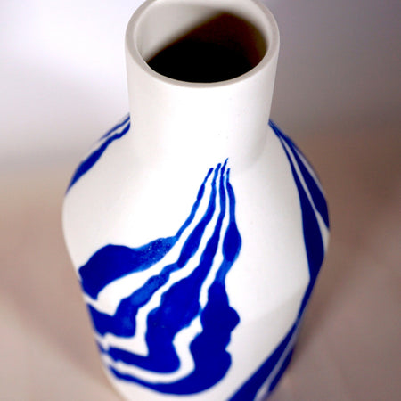 the neck of a porcelain white bottle vase with a bright blue leaf pattern. 