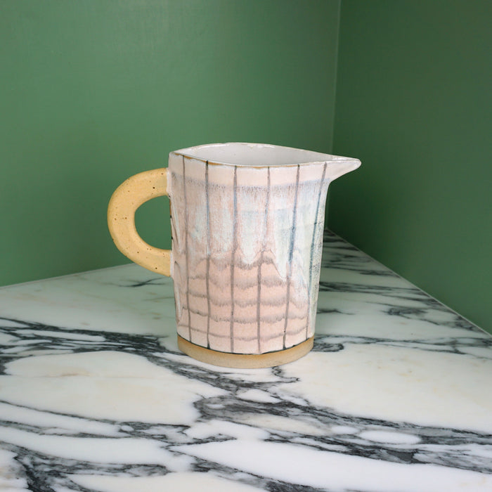 handmade jug with a crosshatch pattern and yellow handle on a marble table with a green background. 