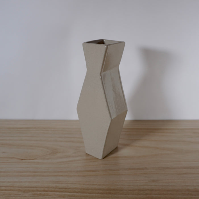 side view of an angular handmade vase. its long and tall and simple in its design. 