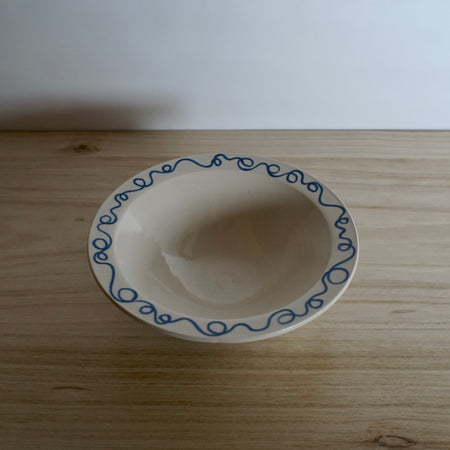 a handmade ceramic pasta bowl on a wooden table with a blue line drawing on the rim. 