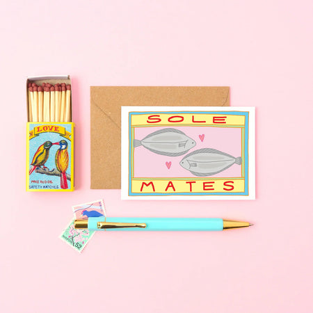 a small card with two fishes and a message that reads Sole mates spelt S O L E. next to a match box and a pen. 