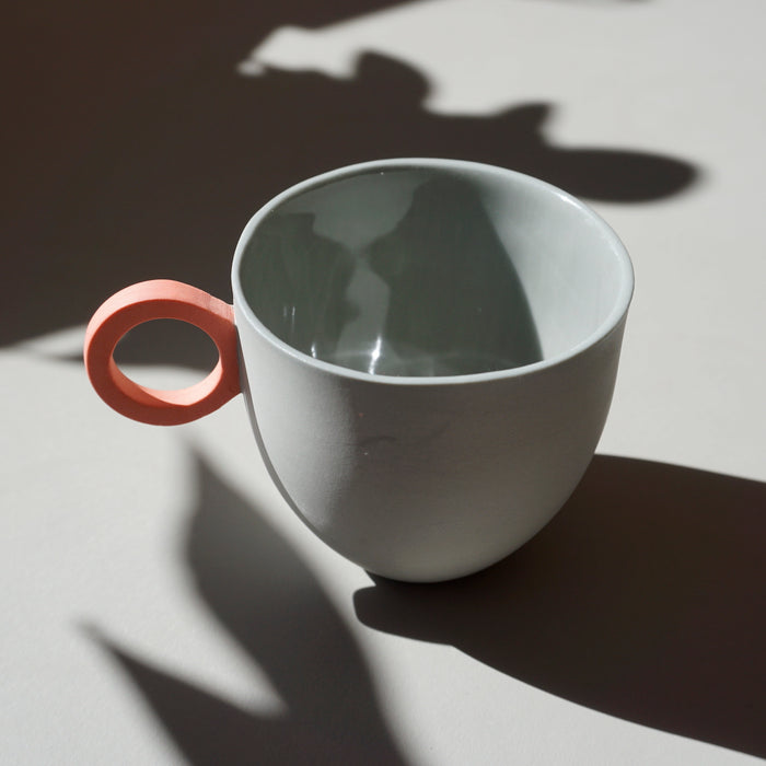 a round grey espresso cup with a pink handle. 