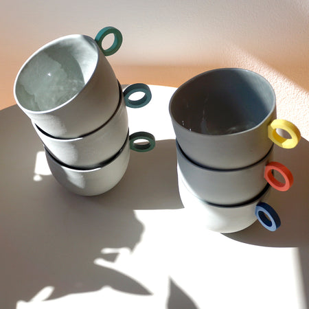 6 round grey cups in two stacks of three. all with different colour handles. 