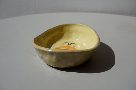 a side view of a soap dish by beci callow that looks like an avocado cut in half with a face painted on to the bottom. 