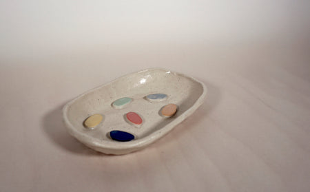 a light coloured ceramic soap dish with multi coloured dots on the bottom. 