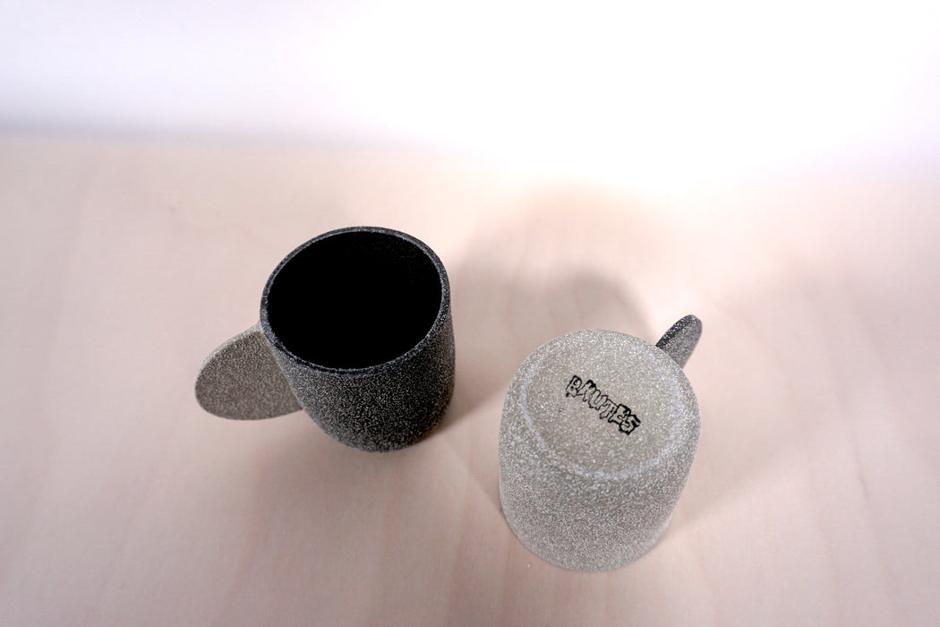 two grey espresso cups on a light background. one is lighter than the other and is upside-down so you can see the Brutes Ceramics makers mark.  