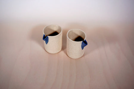 two sand coloured small jugs with denim blue spouts on a light background. 