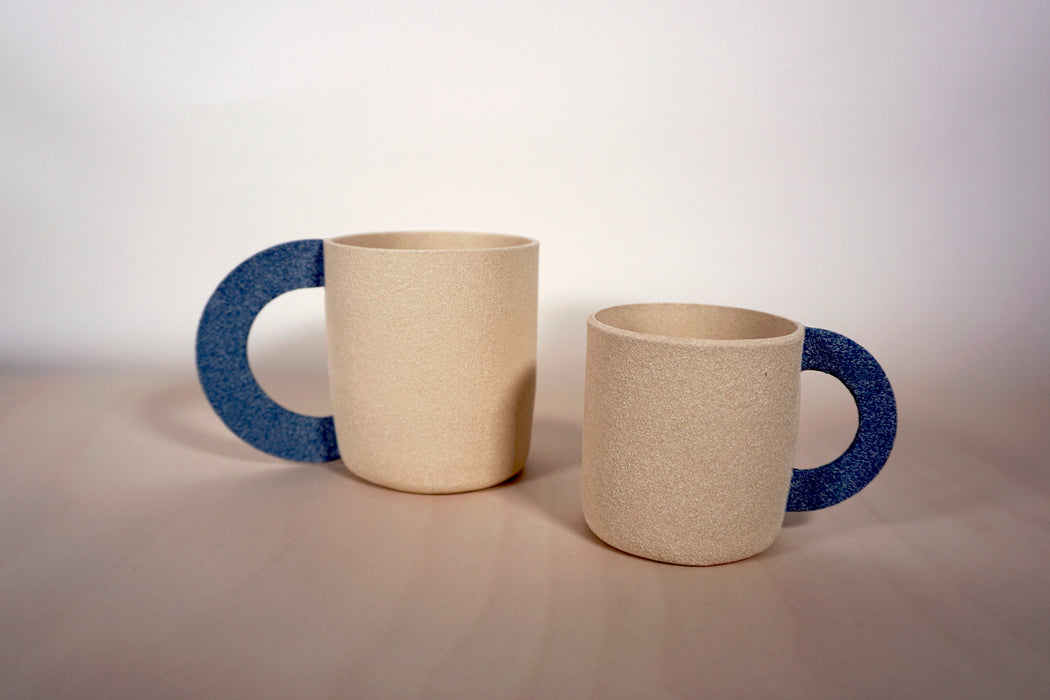 a large mug and a smaller mug. both sand coloured clay with a half moon blue denim handle. 