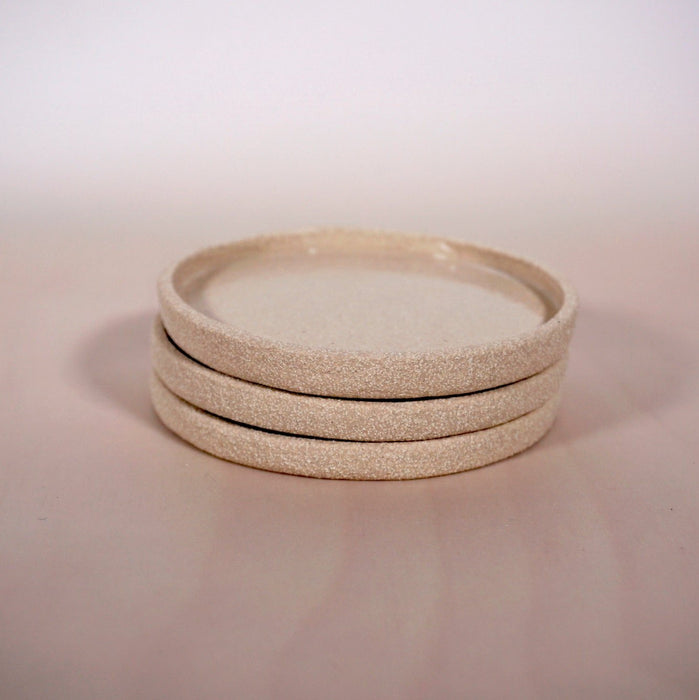 three light clay saucers in a stack on a light coloured background. 