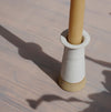 closeup of a Cara Guthrie candlestick holder in white with a yellow beeswax candle. 