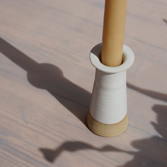 closeup of a Cara Guthrie candlestick holder in white with a yellow beeswax candle. 