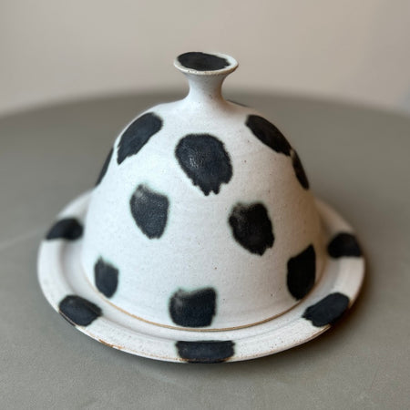 a round butter dish that is white with dark spots all over it. 