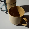 close up of a oatmeal coloured mug with two other mugs in the background. 