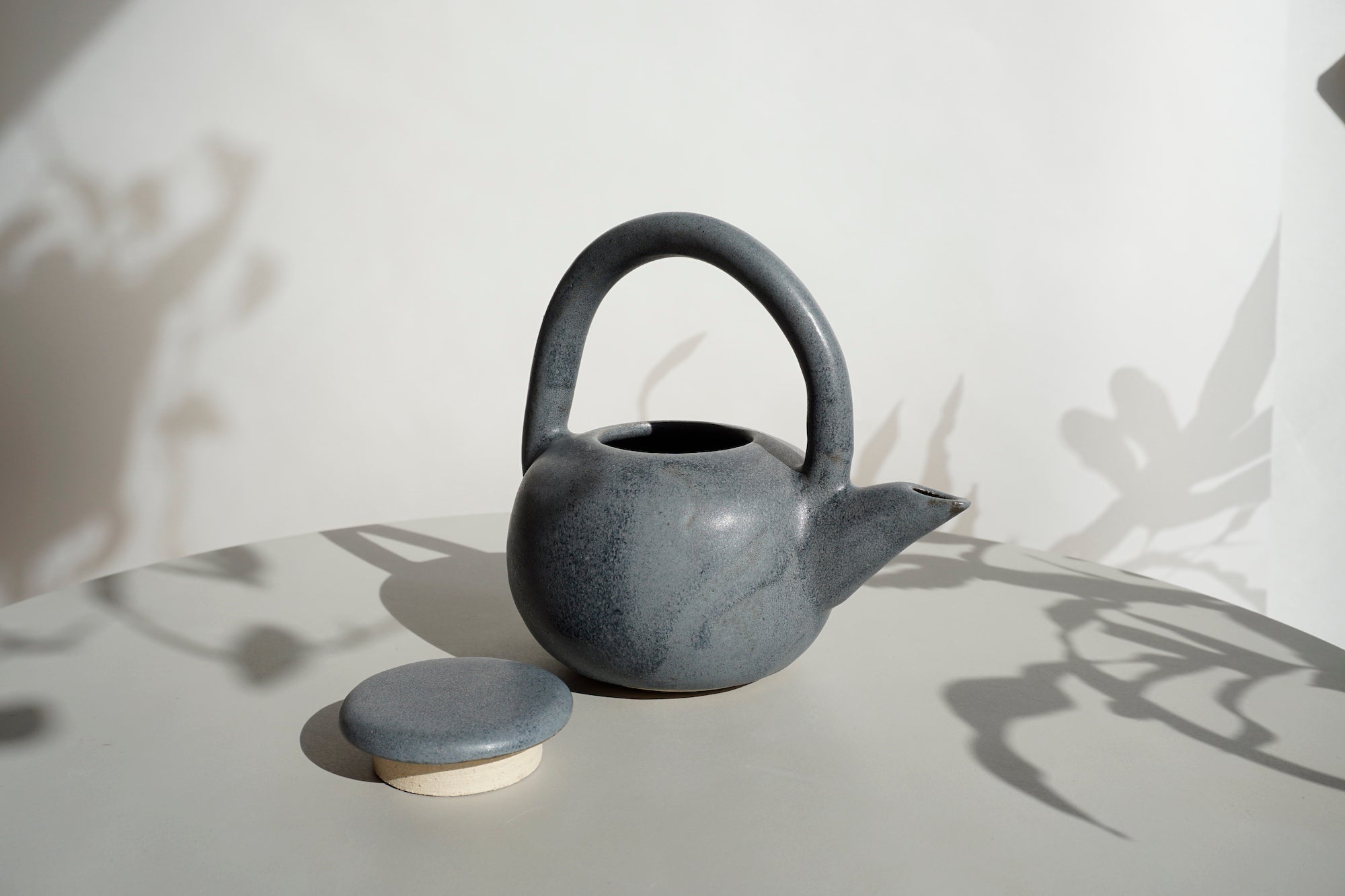 a teapot on a light grey table with the lid sitting next to it. 