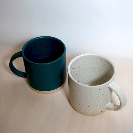 a dark green mug and a white mug on a wooden surface. 